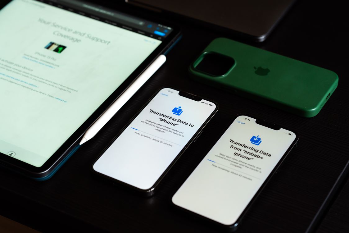 Two iPhones transferring data beside an iPad on a desk